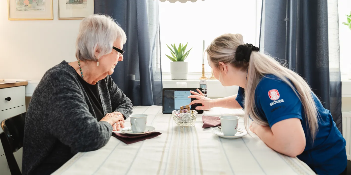 En äldre kvinna sitter sitter och tittat på ipad tillsammans med personal.