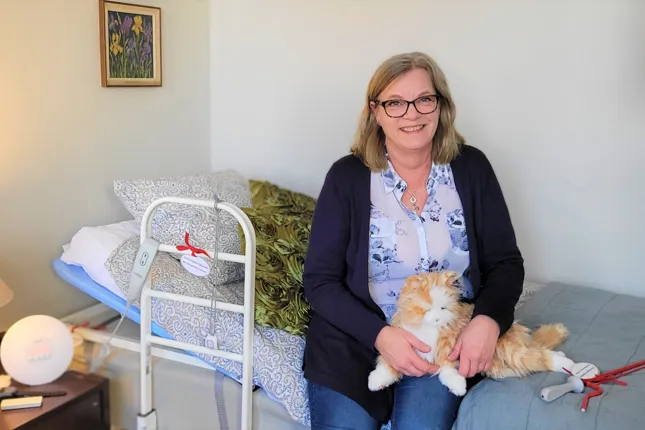 En kvinna sitter på en säng och håller i en katt.