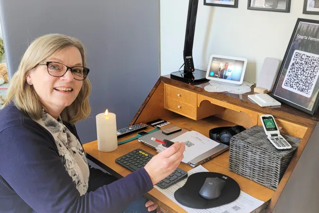 En kvinna sitter vid ett skrivbord med en mobiltelefon.
