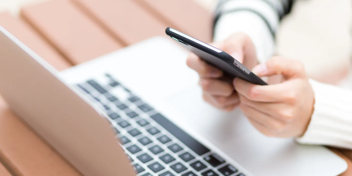 En person som använder en mobiltelefon medan hen sitter framför en bärbar dator