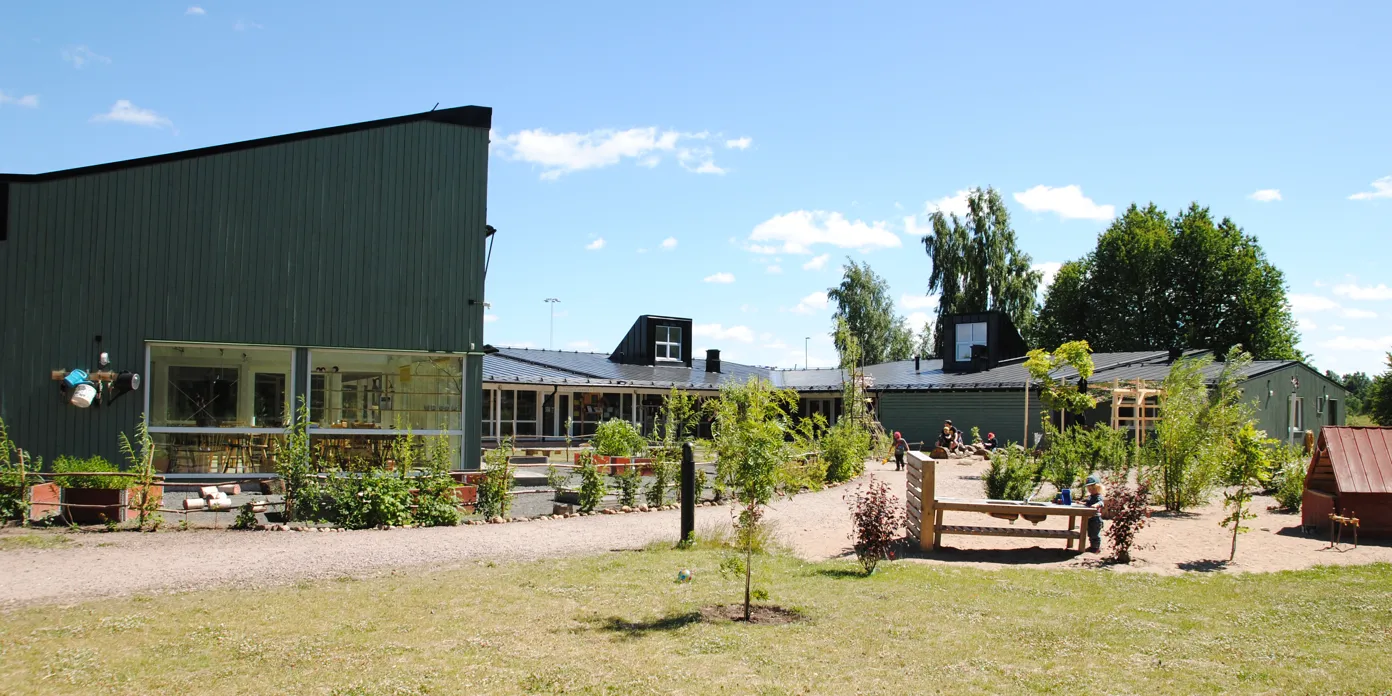 En grön byggnad med många träd framför sig