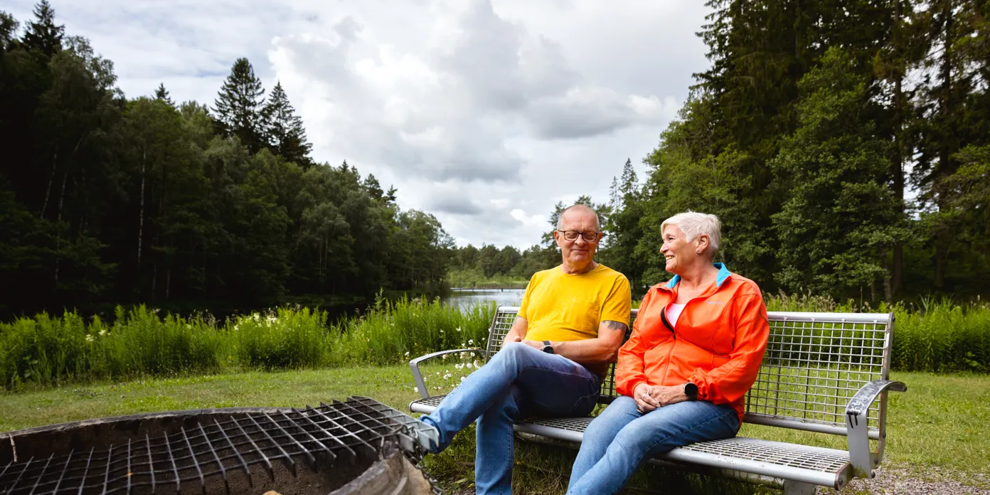 En man och en kvinna sitter på en bänk bredvid en grill
